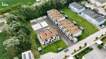 Luftaufnahme von modernen Reihenhäusern mit Gründächern und angrenzenden Parkplätzen in ländlicher Umgebung.