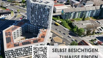 Luftaufnahme eines modernen Gebäudekomplexes mit markanter Architektur, Solarpaneelen auf den Dächern und städtischer Umgebung.
