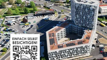 Luftaufnahme eines modernen Gebäudes mit markanter geometrischer Fassade, Solarpaneelen auf dem Dach und einem Innenhof in städtischer Umgebung.