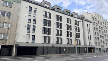 Moderne Wohngebäude-Fassade mit vielen Fenstern und Dachgauben an einer Stadtstraße.