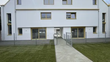Moderne weiße Fassade eines Wohngebäudes mit gelben Fensterrahmen und einem gepflegten Vorgarten.
