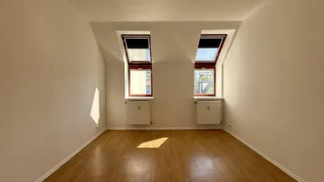 Heller Raum im Dachgeschoss mit Holzfußboden, weißen Wänden und zwei Dachfenstern.