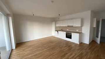 Heller, offener Wohnbereich mit integrierter Küche, Parkettboden und Zugang zum Balkon.