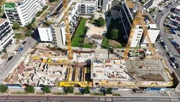 Luftaufnahme einer Baustelle mit Kränen, umgeben von modernen Wohngebäuden und städtischer Infrastruktur.