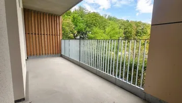 Geräumiger Balkon mit Betonboden, Metallgeländer und Holzverkleidung, bietet einen Blick ins Grüne.