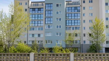 Moderne Wohnhausfassade mit großen Fenstern und Balkonen in einem städtischen Umfeld.