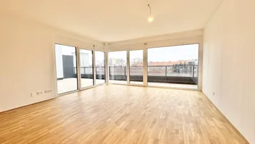 Helles, leeres Wohnzimmer mit großen Fenstern und Zugang zu einer Terrasse, ausgestattet mit Parkettboden.