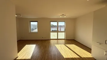 Helles Wohnzimmer mit Parkettboden und Zugang zu einem Balkon oder einer Terrasse, durchflutet von Tageslicht.
