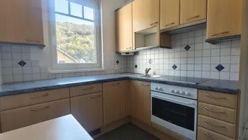 Funktionale Küche mit Holzschränken, Fliesenrückwand und Blick ins Grüne vom Fenster aus.