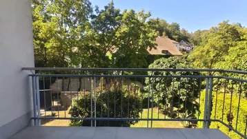 Heller Balkon mit Fliesenboden und weitem Blick ins Grüne und auf umliegende Häuser.