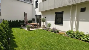 Gepflegter Gartenbereich mit Rasenfläche, Hecke und möblierter Terrasse für entspannte Stunden im Freien.