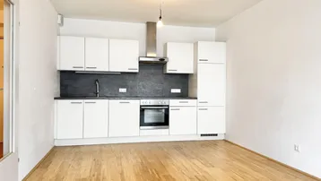 Moderne Einbauküche mit weißen Schränken, dunkler Arbeitsplatte und Holzboden in einem hellen Raum.