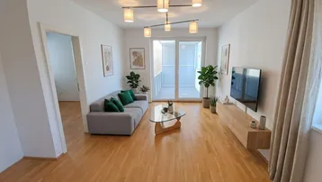 Helles Wohnzimmer mit Parkettboden, moderner Einrichtung und Zugang zu einem Balkon.