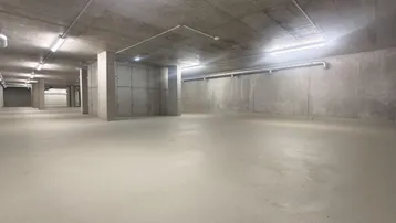 Großer, leerer Raum im Untergeschoss mit Betonwänden und -decke, beleuchtet mit Leuchtstoffröhren.