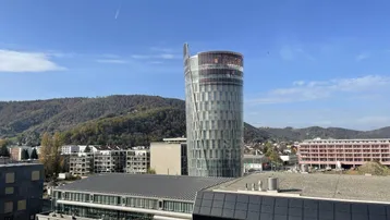 Panoramablick auf die Stadt mit moderner Architektur und bewaldeten Hügeln im Hintergrund.