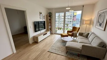 Helles Wohnzimmer mit modernem Sofa, Holzboden und Zugang zu einem Balkon.