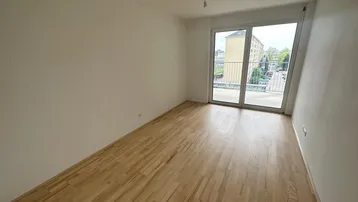 Helles, leeres Zimmer mit Parkettboden und Zugang zu einem französischen Balkon, ideal für individuelle Gestaltung.