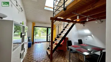 Heller Wohn- und Essbereich mit Holztreppe zur Galerie und Zugang zum Garten.