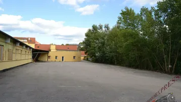 Großer asphaltierter Außenbereich mit angrenzenden Gebäuden und viel Grünfläche unter blauem Himmel.
