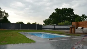 Großer Gartenbereich mit eingelassenem Pool und gefliester Terrasse, umgeben von einem modernen Zaun.