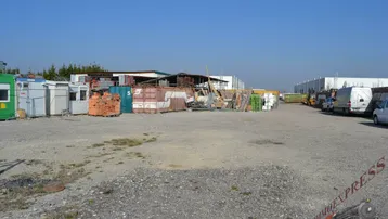 Weitläufiges Außengelände mit Lagerflächen, Containern und Baumaterialien unter blauem Himmel und Sonnenschein.