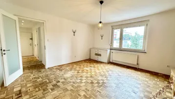 Helles Wohnzimmer mit Parkettboden, weißen Wänden und einem Fenster, das viel Tageslicht hereinlässt.