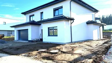 Neubau-Einfamilienhaus mit weißer Fassade, dunklen Fenstern und integrierter Garage, umgeben von unfertigem Gelände.