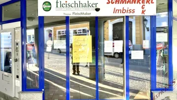 Eingangsbereich eines Geschäfts mit großen Glasfenstern und blauen Rahmen, reflektiert die Umgebung.