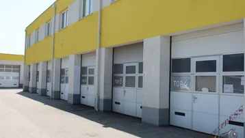 Außenansicht eines Gebäudes mit mehreren Garagentoren und gelb-weißer Fassade unter blauem Himmel.
