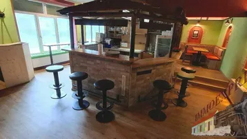 Geräumiger Barbereich mit Holzboden, Theke und Barhockern, ideal für gesellige Runden und helle Atmosphäre.