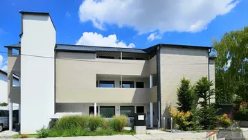 Modernes Mehrfamilienhaus mit heller Fassade und Balkonen unter blauem Himmel.