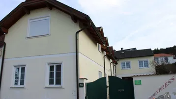 Ansicht der Hausfassade mit Eingangsbereich und Zufahrtstor unter bewölktem Himmel.