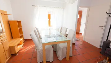 Heller Essbereich mit Terrakottafliesen, großem Glastisch und Zugang zum Flur.