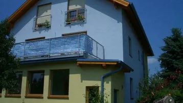 Hausfassade mit Balkon, französischen Balkonen und Satteldach unter blauem Himmel.