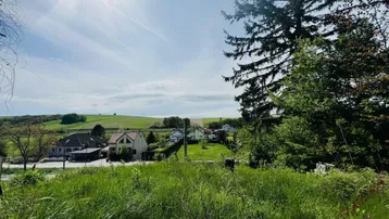Weitläufiger Blick über grüne Hügel und die umliegende ländliche Bebauung unter blauem Himmel.
