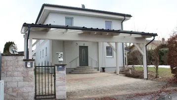Vorderansicht des Hauses mit Carport und gepflasterter Auffahrt.
