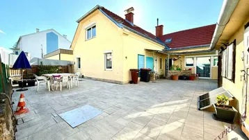 Große gepflasterte Terrasse mit Gartenmöbeln und Blick auf das Haus unter blauem Himmel.