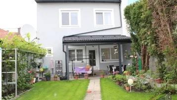 Hinterhof mit gepflegtem Rasen, überdachter Terrasse und blühenden Pflanzen, ideal zum Entspannen.