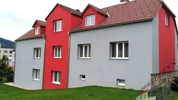 Ansicht eines modernen Mehrfamilienhauses mit auffälliger rot-grauer Fassade und gepflegtem Vorgarten.