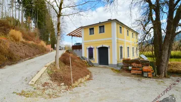 Gelbes Gebäude mit traditioneller Architektur, umgeben von Natur und einem Schotterweg.