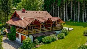 Rustikales Haus mit Holzbalkonen und rotem Ziegeldach, umgeben von üppigem Grün und hohen Bäumen.