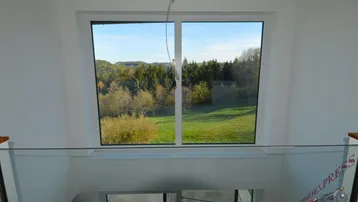 Offener Flurbereich mit Glasgeländer und weitem Blick in die Natur durch das große Fenster.