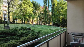 Blick vom Balkon auf eine grüne Gartenanlage mit Bäumen und Rasenfläche.