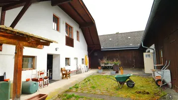 Innenhof mit Rasenfläche und Gartenutensilien zwischen zwei Gebäudeteilen, umgeben von Holzfassaden.
