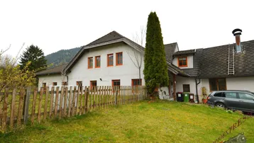 Ländliches Wohnhaus mit weißer Fassade, Holzzaun und großem Gartenbereich, umgeben von grüner Natur.