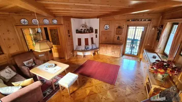 Wohnbereich mit Holzboden, bequemen Sesseln und einem traditionellen Kachelofen in der Ecke.