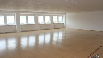Großer, heller Büroraum mit vielen Fenstern und hellem Holzfußboden, ideal für offene Arbeitsbereiche.