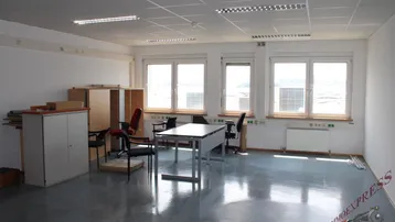 Geräumiges Büro mit grauem Betonboden, großen Fenstern und einfacher Büroeinrichtung.