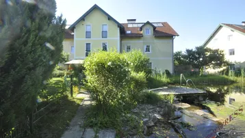 Großzügiger Gartenbereich mit Teich und Steg, umgeben von viel Grün und dem Haus.