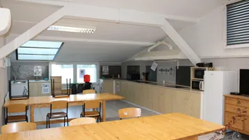 Große Gemeinschaftsküche mit mehreren Esstischen, Holzbalken und Dachfenstern.